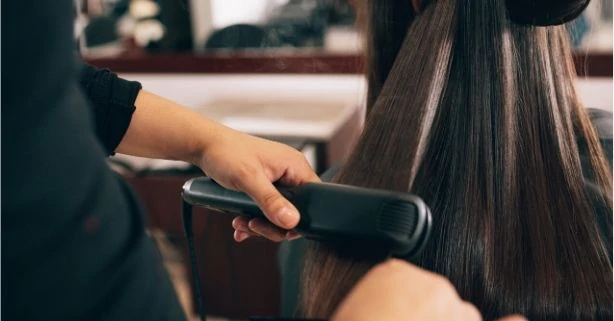 woman having her hair straightened with a flat iron for dry damaged hair