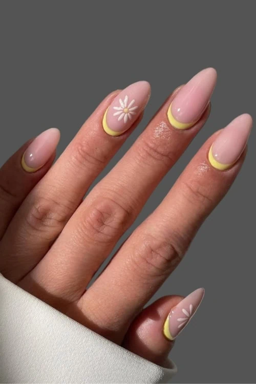 female hand with yellow and nude manciure with white flower