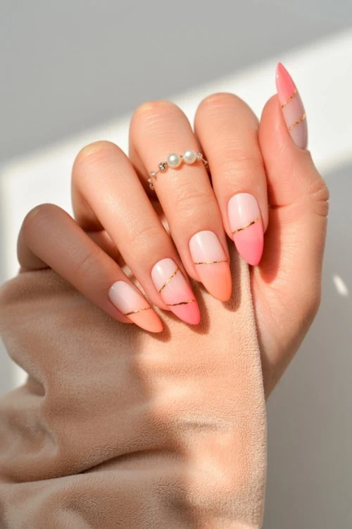 hand with peach and pink ombre nails with gold accent