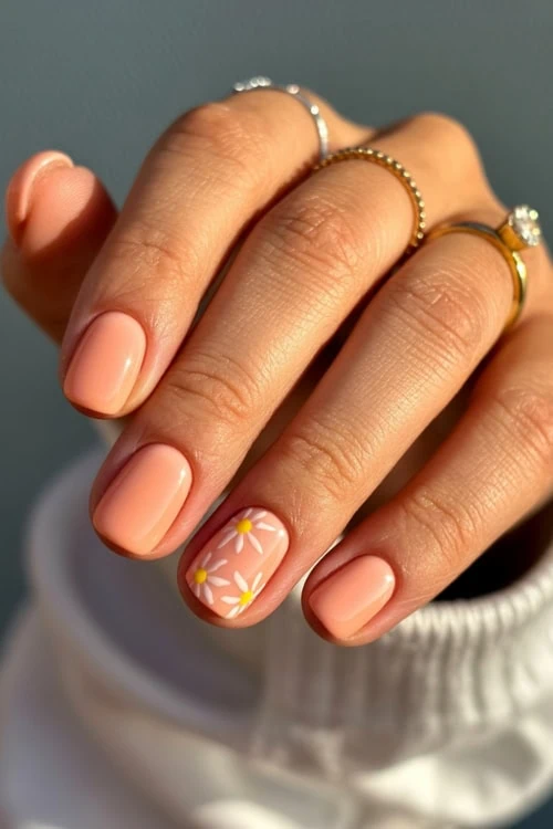 hand with short peach nails with daisy nail art