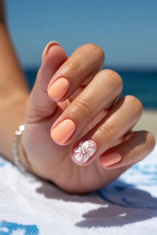 hand with short peach nails with white floral accent on the beach
