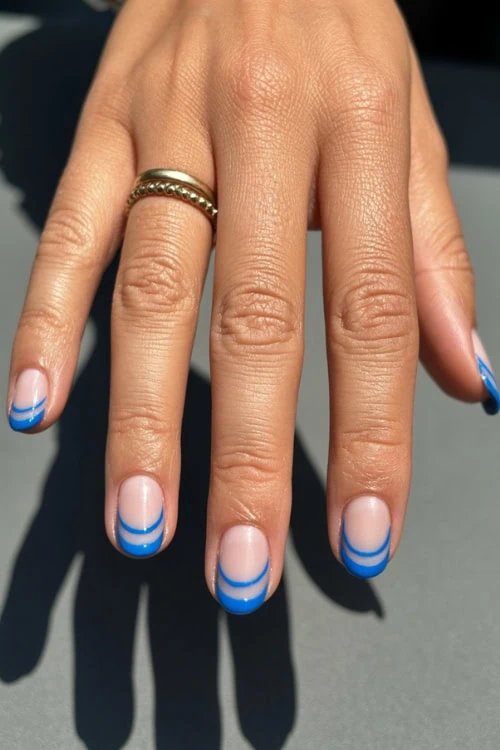 hand with french tip nails that are blue and use negative space design