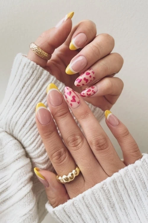 female hand with mustard yellow french tip nails design and hearts