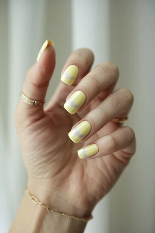 female hand with pale yellow nail manicure and horizontal nails design