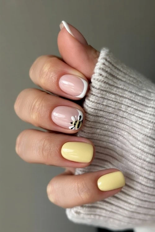 hand with pastel yellow nails design featuring a bumble bee