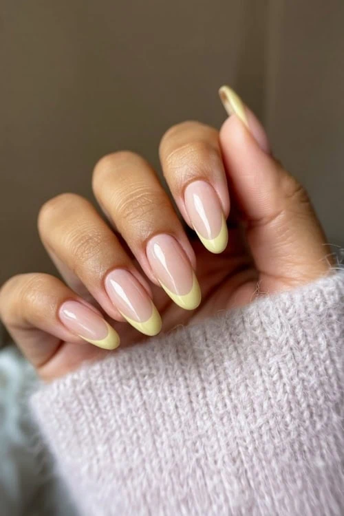 female hand with butter yellow french tip nails
