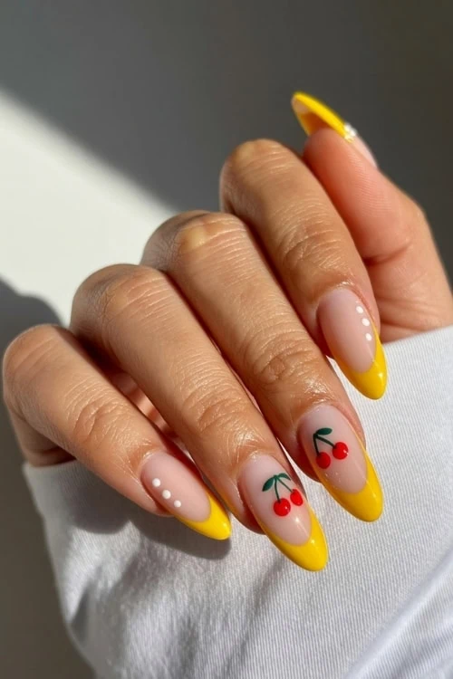 hand with yellow french tip nails with cherries and white polka dot nail design