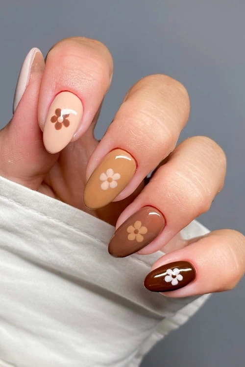 female hand with brown and neutral colored nails for fall with daisies on each
