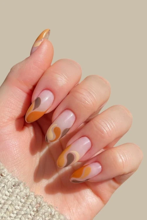 Woman's hand with fall nails design with classic fall colors like burnt orange, brown, and mustard yellow