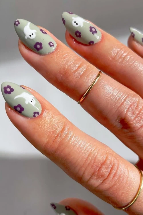 female hand with gray nail polish and tony flowers with ghosts painted on them for halloween