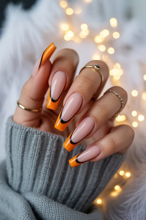 female hand with orange french tip nails with black for halloween