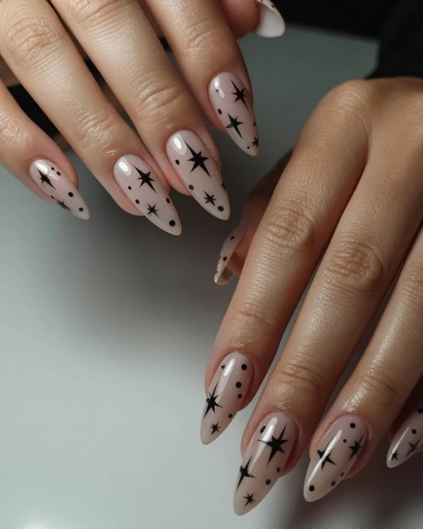 Elegant nude stiletto nails with black star and dot celestial nail art design, perfect for stylish everyday or special occasion manicures.