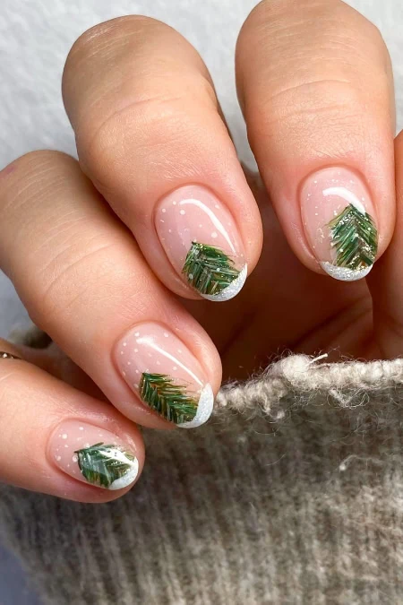 Festive Christmas nail art with green pine tree designs and white tips on natural nails, perfect for holiday season beauty and manicure inspiration.