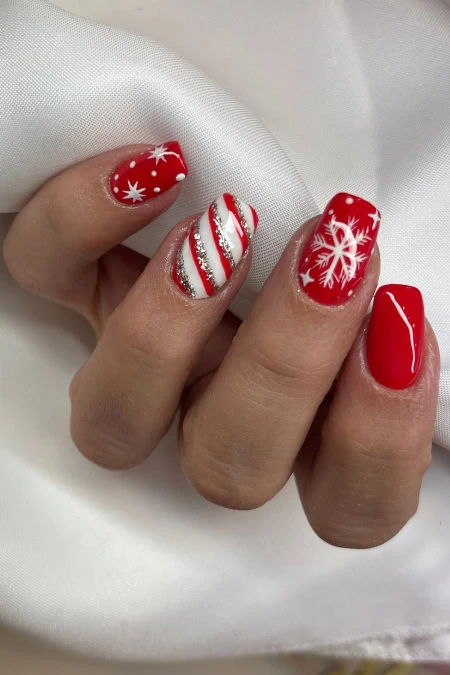 Festive red nail art with white snowflakes, candy cane stripes, and holiday-themed designs