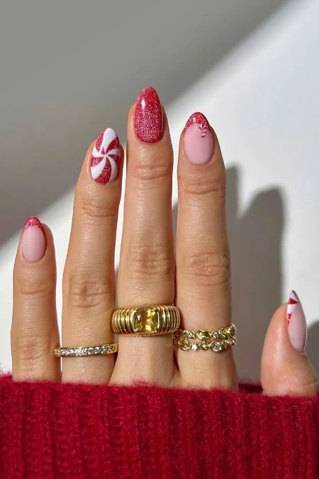 Festive holiday-themed manicured nails with peppermint candy nail art and sparkling red glitter polish, showcasing stylish and seasonally Christmas inspired nail art design.