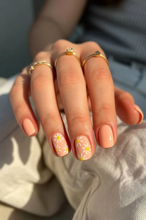 Elegant manicured nails with daisy flower nail art and gold rings, perfect for spring or summer beauty trends.