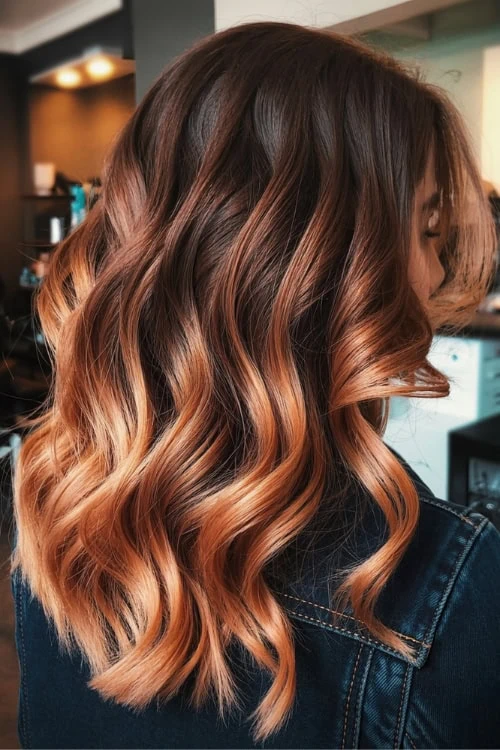 Vibrant balayage fall hair color with caramel highlights and soft waves, perfect for a trendy, salon-quality look.