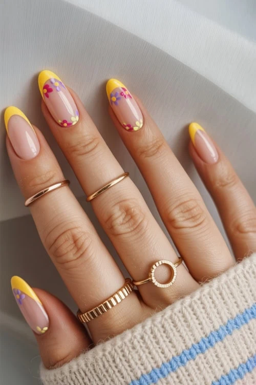 Colorful floral French manicure with yellow tips and floral accents on nails, elegant hand jewelry, perfect for spring or summer beauty and nail design art inspiration.