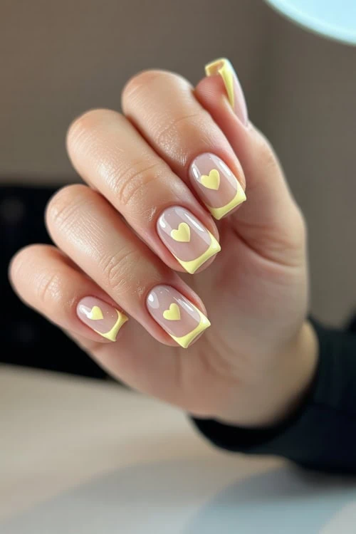 Vibrant yellow French manicure with heart accents on natural nails, perfect for a stylish and romantic look, by The Beauty Deep Life.