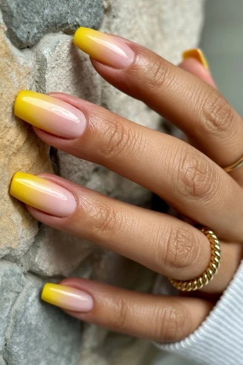 Vibrant yellow French manicure with glossy finish on natural nails, close-up of hand with gold ring, emphasizing nail art and beauty care.