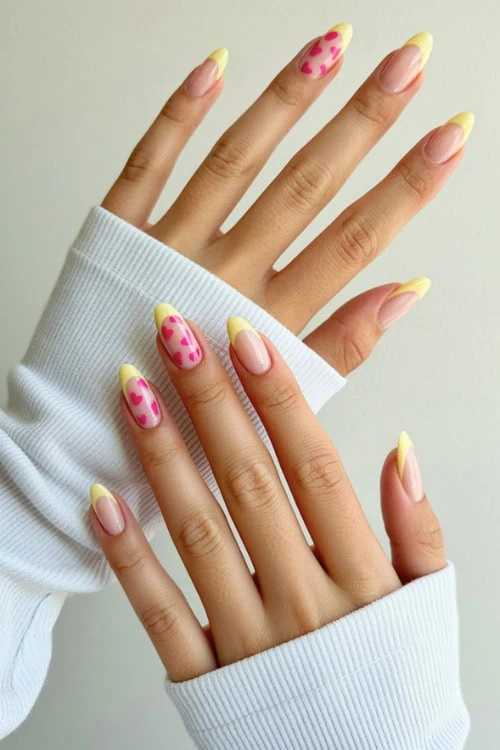Vibrant yellow and pink heart-patterned nail art on manicured fingers featuring gel nail polish and trendy nail design.