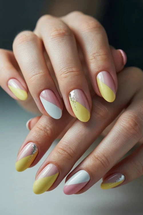 Bright pastel yellow and white nail art with glitter accents on manicured hands, perfect for a trendy, stylish look.