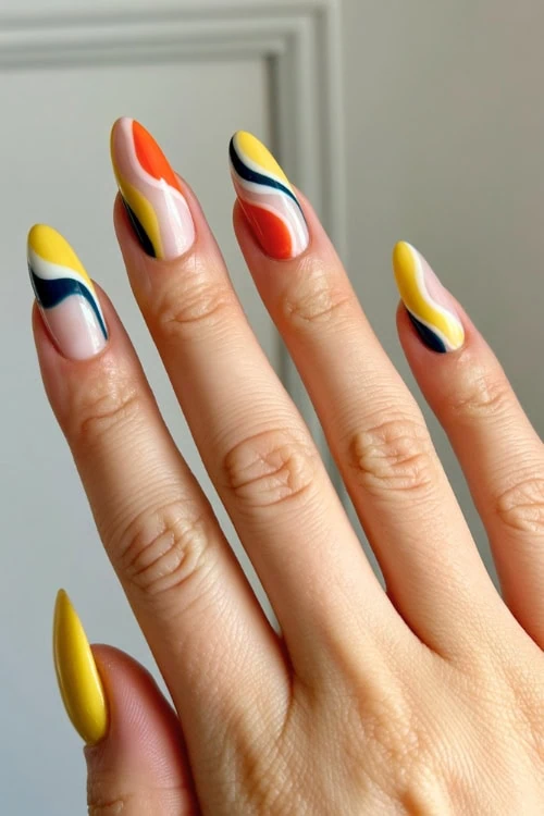 Colorful abstract nail art with yellow, blue, white, and orange streaks on long manicured nails.