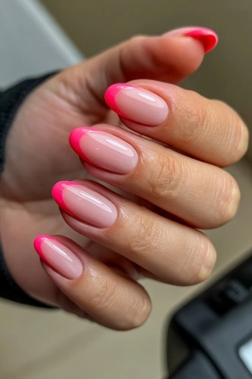 Bright pink French tip manicure with glossy finish on natural nails for a trendy and elegant look.