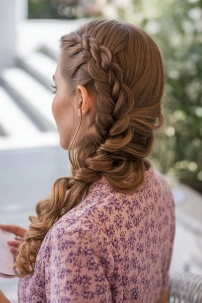 Intricate braided hairstyle with loose curls in a natural outdoor setting, showcasing elegant hair styling for special occasions or everyday beauty routines.