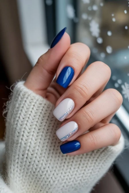 Vibrant blue and elegant white snowflake nail art on manicured fingernails with glitter accents, perfect for winter beauty and holiday manicure trends.