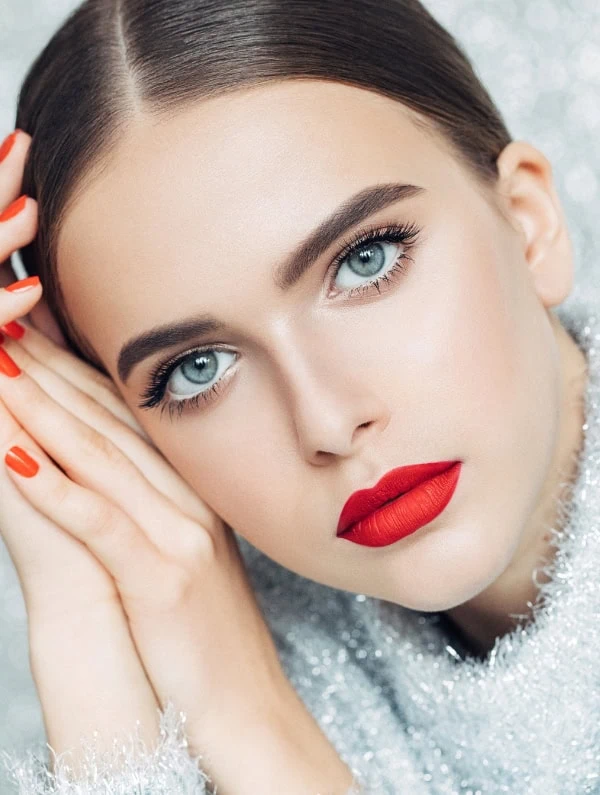 Stunning woman with flawless makeup, bold red lipstick, bright blue eyes, and perfectly shaped eyebrows, showcasing beauty and makeup look for Christmas