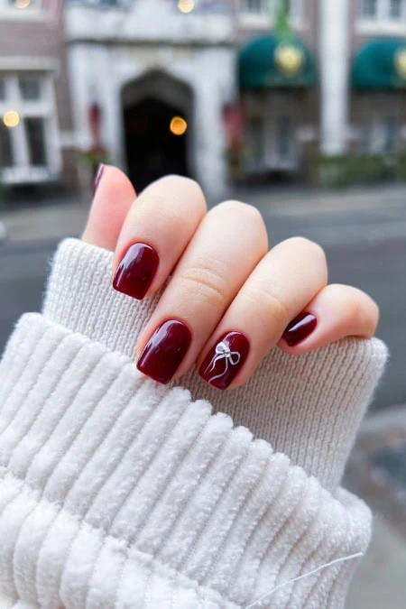 Red and white Christmas-themed nail art with a bow design on the ring finger, perfect for holiday nail fashion and beauty trends.