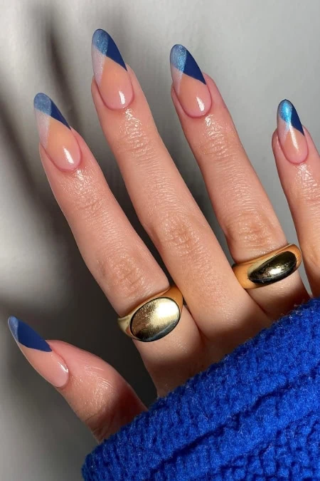 Vivid blue and nude French manicure with glossy finish, decorated with gold rings on fingers, showcasing elegant and trendy nail art for beauty and fashion enthusiasts.
