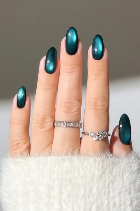 Vibrant teal metallic gel manicured nails with elegant rings on a woman's hand, showcasing luxury nail art and jewelry for a stylish, beauty, and fashion-focused look.