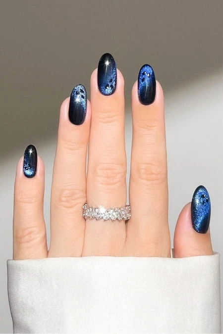 Vibrant galaxy-inspired blue and black nail art with glitter accents on manicured fingernails.