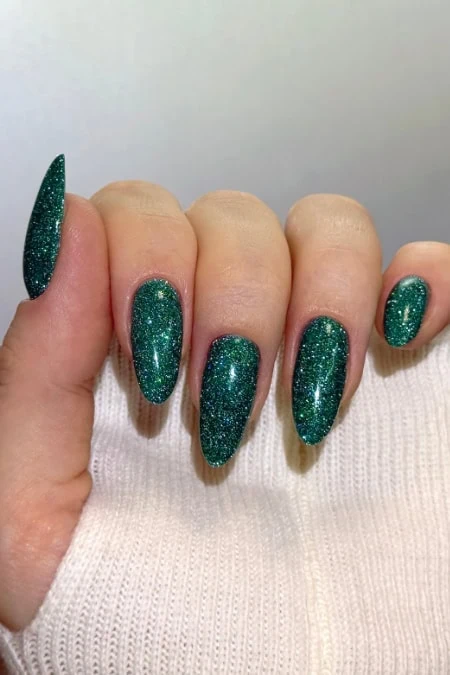 Vibrant green glitter nail polish on manicured nails, perfect for a stylish and glamorous winter look.