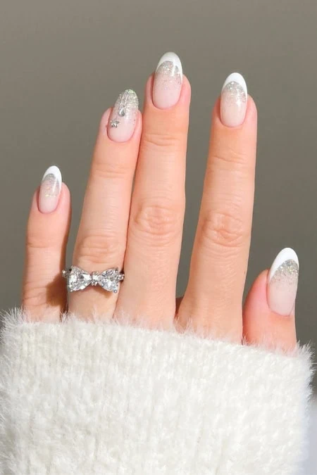Elegant manicured nails with white French tips and glitter accents, featuring a diamond engagement ring on the finger, showcasing winter nails.