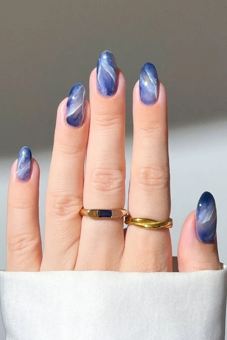 Vibrant blue marble nail art on well-manicured fingernails with stylish rings, perfect for a trendy nails look.