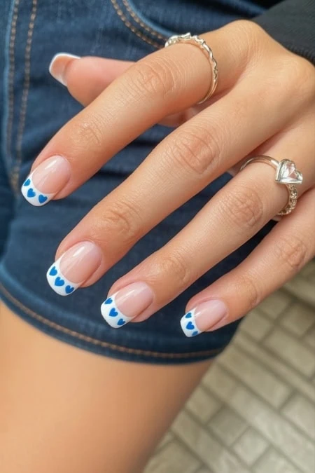 Elegant hand with blue heart nail art and rings, showcasing trendy nail design and jewelry for women’s beauty, style, and accessories.
