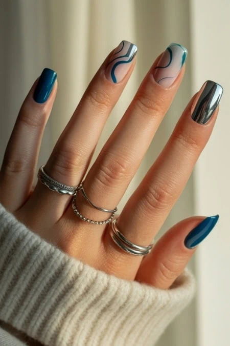 Shiny blue and marble nail art on well-manicured hands with rings, showcasing trendy, sophisticated manicures for beauty and new years.