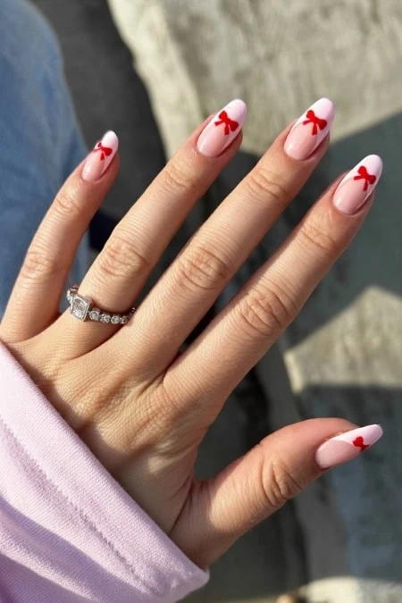 Red bow nail art design with a glossy finish on a manicured hand holding a ring.