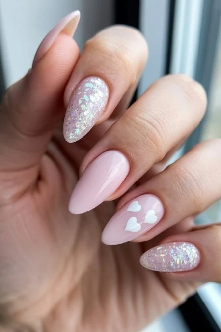Elegant pastel pink almond-shaped nail art with white heart accents and iridescent glitter accent nails, perfect for a stylish and cute Valentine's manicure look.