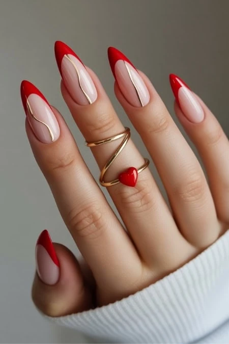 Stylish Valentine's nails with red and nude polish, featuring gold accents and a heart-shaped ring on a manicured hand.