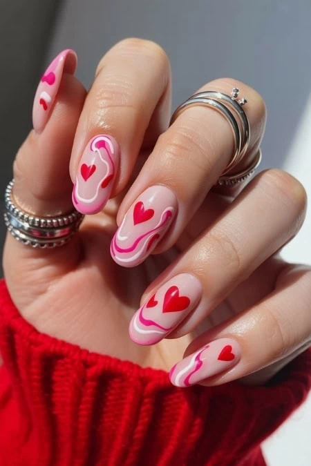 Red and pink heart-themed Valentine's Day nail art with swirl design, perfect for love and special occasions.
