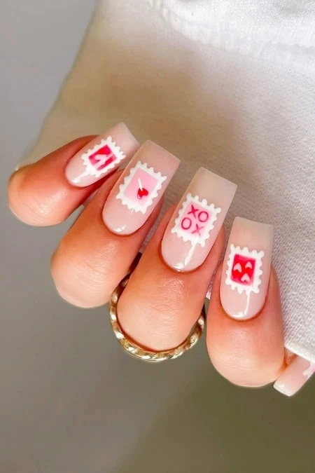 Cute Valentine's Day nail art with love-themed stamp designs on pastel pink nails, featuring hearts, XOXO, and smiley face stamps for a festive and romantic manicure.