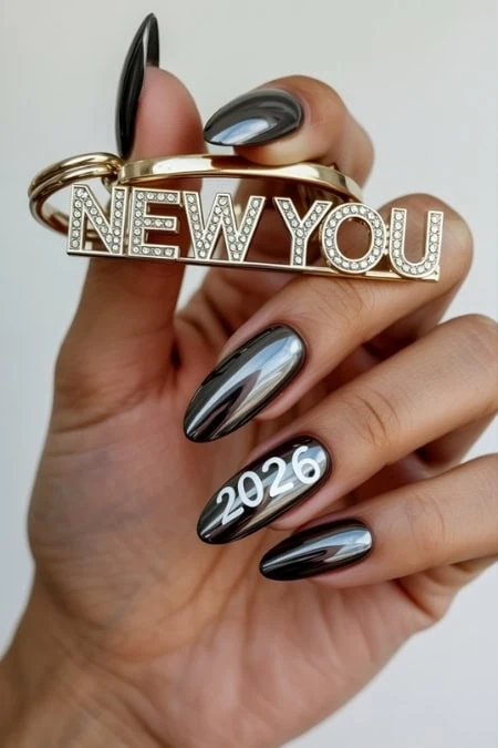 Shiny black polished nails with "2026" and hand holding a gold "New You" keychain for New Years 2026 celebration and self-improvement.