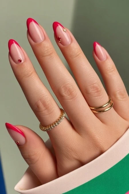 Bright and elegant nail art featuring red French tips with gold accents, showcasing professional manicure and stylish jewelry on well-groomed fingers.
