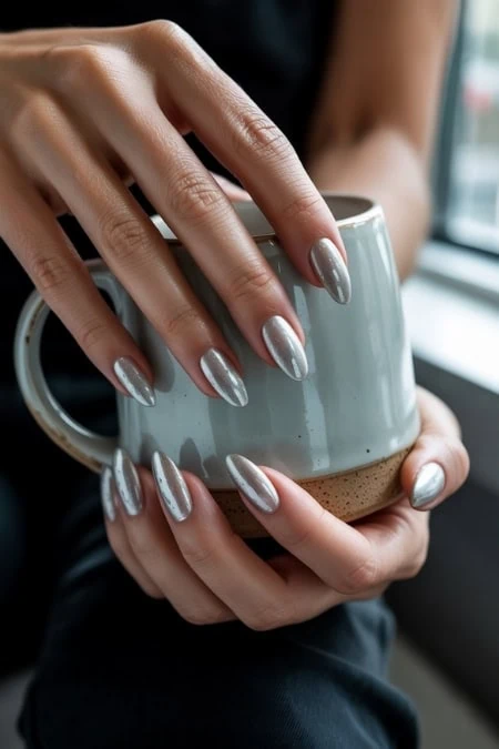 Shiny silver manicured nails holding a ceramic mug, close-up of hand and drink, natural light, lifestyle beauty and self-care image.