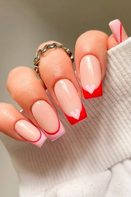 Soft pink and red french manicure with heart accents for romantic nail art, perfect for Valentine's Day or special occasions. Expertly manicured nails with trendy, cute nail design.