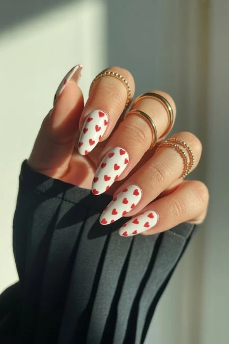 Bright, heart-themed nail art with white base and red hearts, complemented by gold rings on fingers, perfect for stylish, romantic nail design enthusiasts.